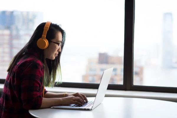 Asian woman wearing headphones using a laptop